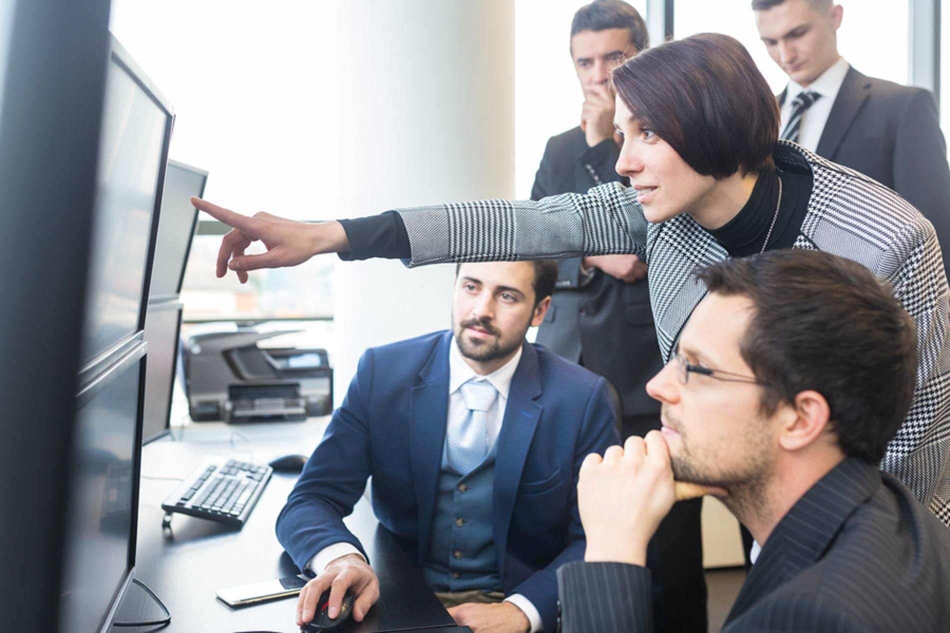 Group of colleagues discussing information displayed on a desktop computer screen.